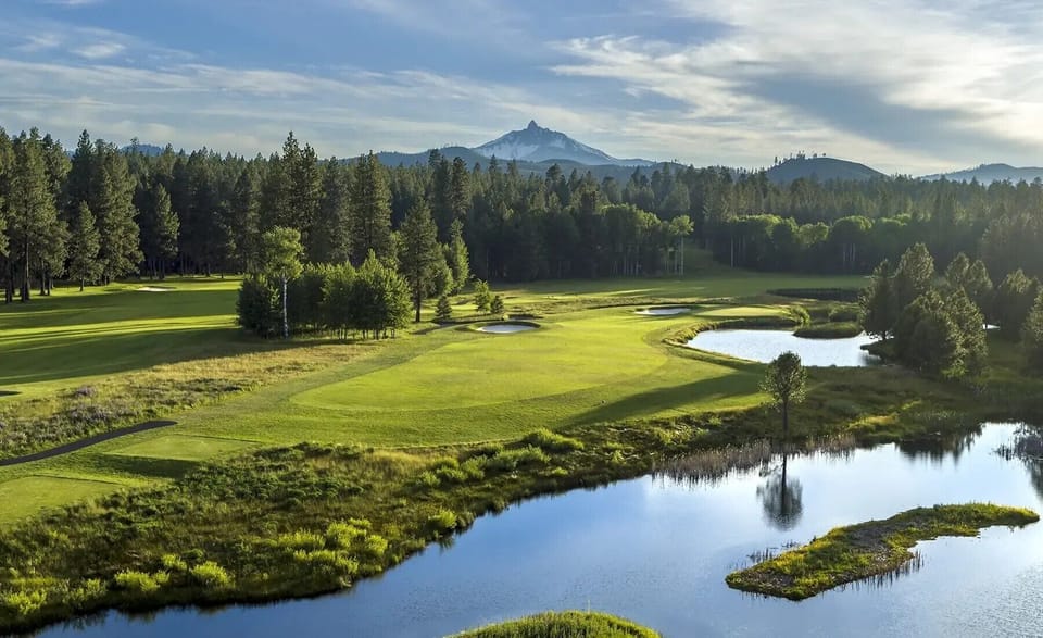 Scenic golf course stretches across pristine landscape with water features and mountain backdrop.