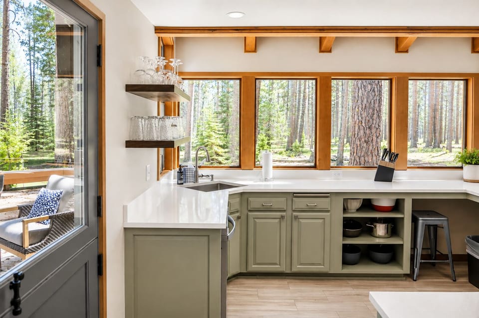 Your modern kitchen opens to serene forest views through expansive windows, blending natural beauty with sleek design for an inspiring culinary experience.