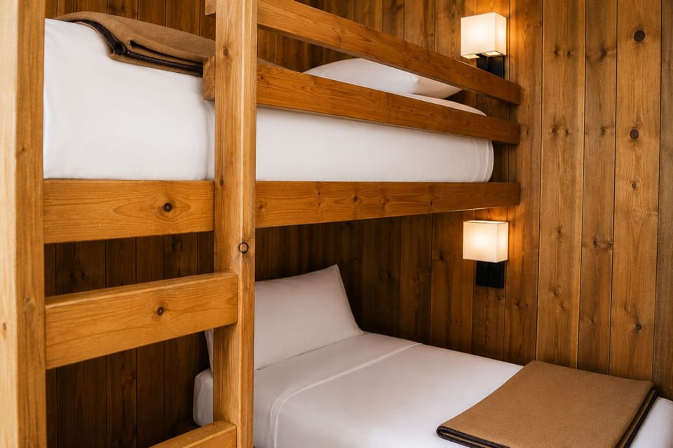 Cozy bunk beds with crisp white linens and warm wood paneling invite you to settle in. Soft reading lights let you unwind at your own pace, creating a welcoming mountain retreat feel.