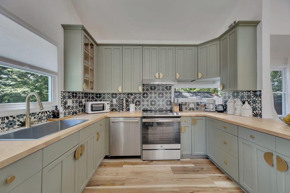 Sleek kitchen w/ sage cabinets, patterned backsplash & stainless steel appliances