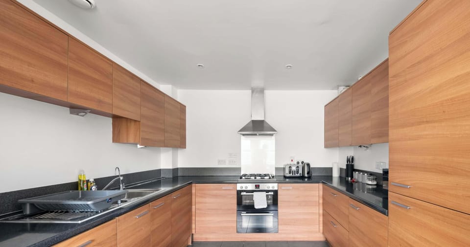 This modern kitchen is designed for both style and efficiency, offering a spacious layout that is perfect for any home cook. The warm wood-finish cabinetry provides a beautiful contrast against the dark slate-grey countertops and large floor.