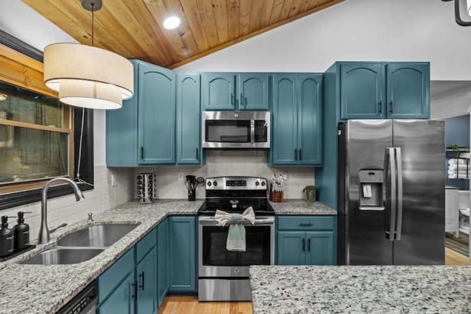 Modern kitchen with teal cabinets, granite counters, and stainless appliances.