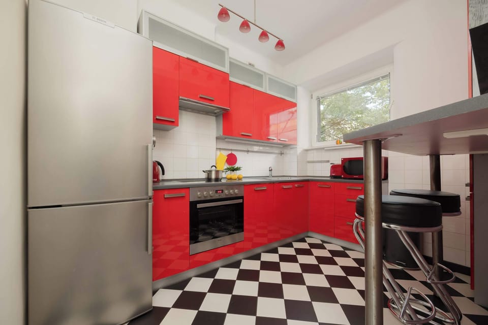 A compact kitchen with red cabinets and black countertops, opening up to a window with natural light.