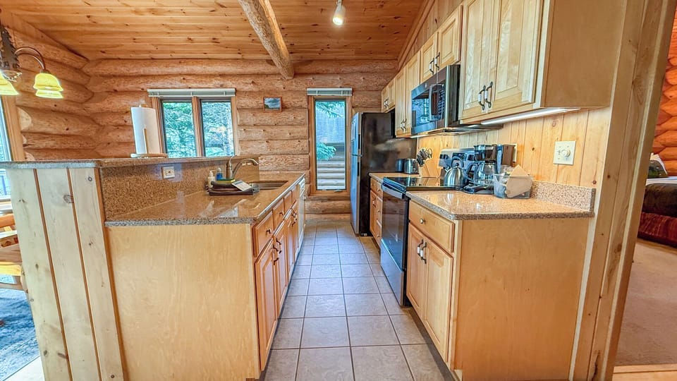 Your fully equipped kitchen awaits with granite countertops, modern appliances, and warm log cabin charm—perfect for preparing meals during your mountain getaway.
