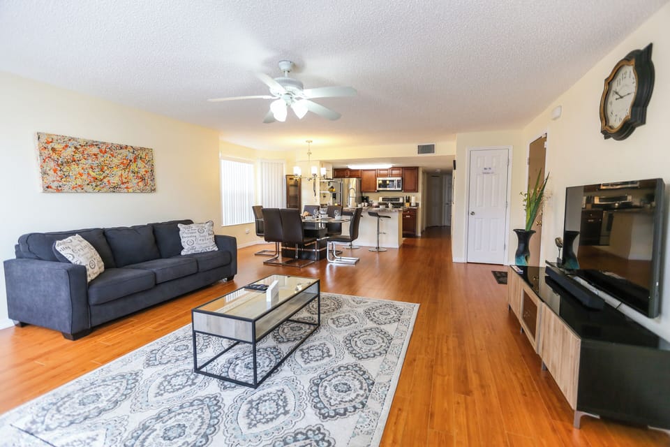 Bright and spacious living area with comfortable seating and a smart TV, featuring an open-concept layout that flows seamlessly into the dining area and fully equipped kitchen—perfect for entertaining and spending quality time together.