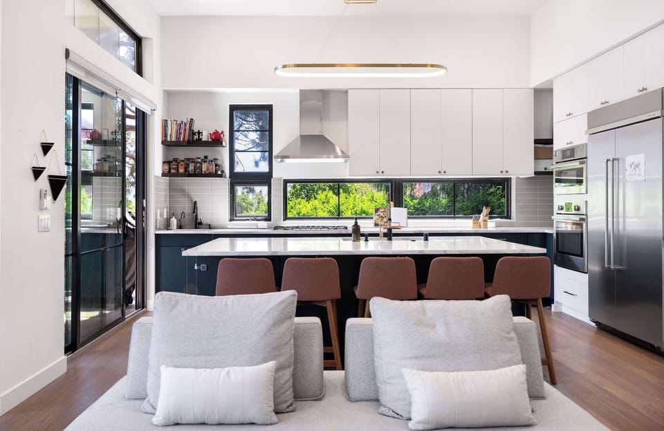 White and navy kitchen with six burgundy stools, stainless appliances, and a cozy living area just beyond.