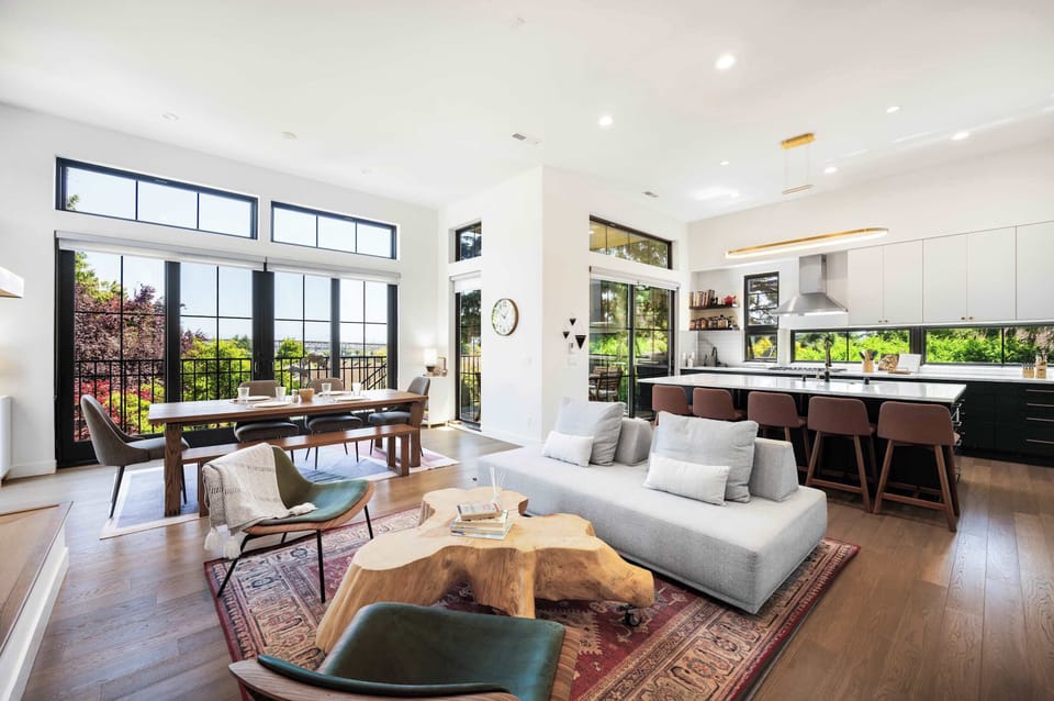 Grey sectional faces a live-edge wood coffee table, with emerald green chairs anchoring the dining space under a statement pendant light.