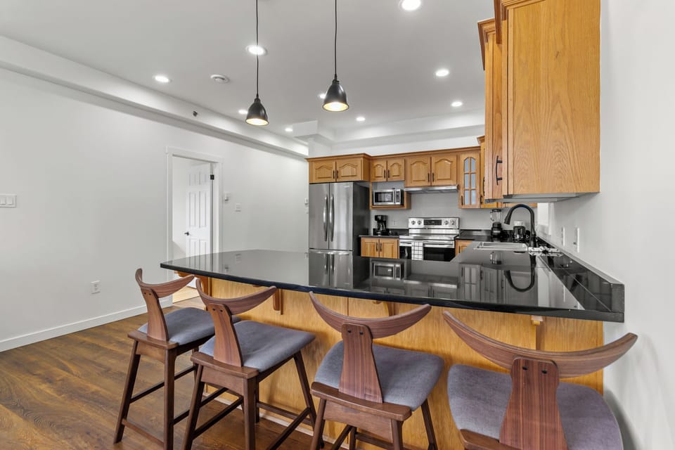 Modern kitchen with sleek black countertops, stainless steel appliances, and warm wooden cabinetry. Ideal for cooking and entertaining.