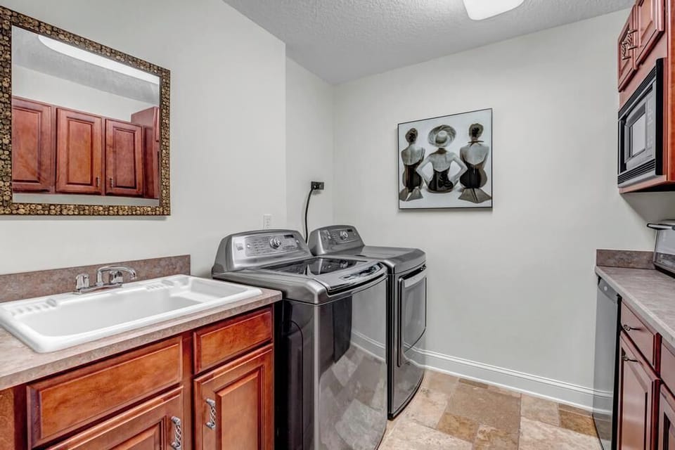 - Full laundry room with modern washer and dryer set plus deep utility sink
- Decorative mirror and bold wall art elevate the look of this workspace
- Custom cabinets and neutral tones blend style with everyday function