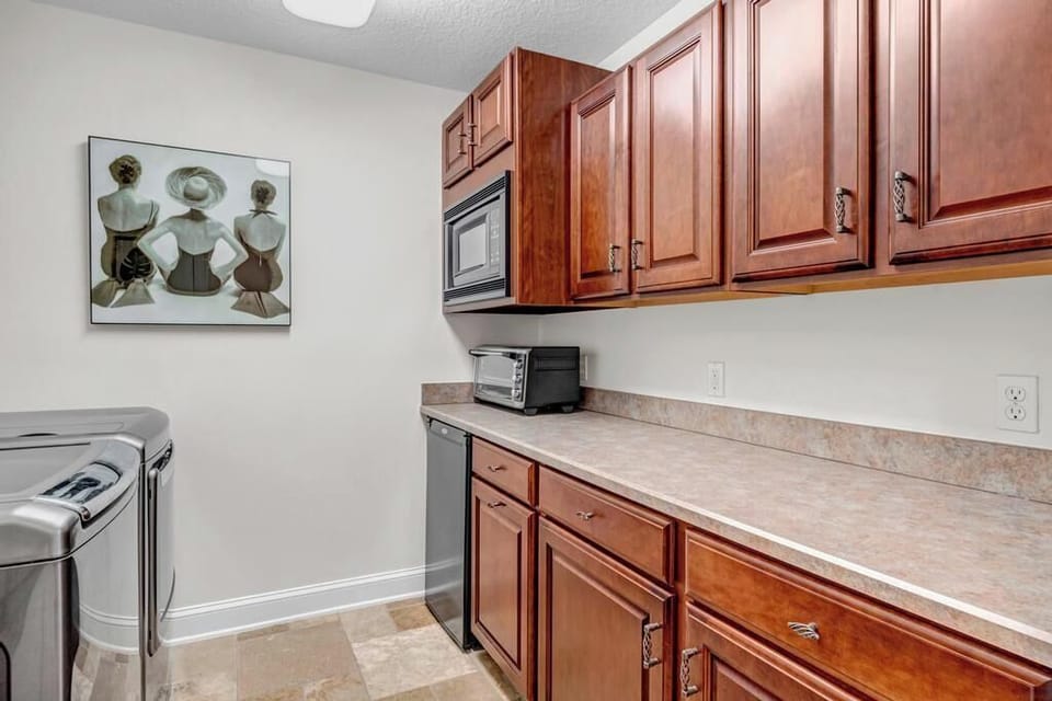- Functional space with rich wooden cabinetry, long countertops, and artwork
- Built in microwave and plenty of surface area for folding and organization
- Sleek appliances and tile floors make laundry tasks smooth and easy