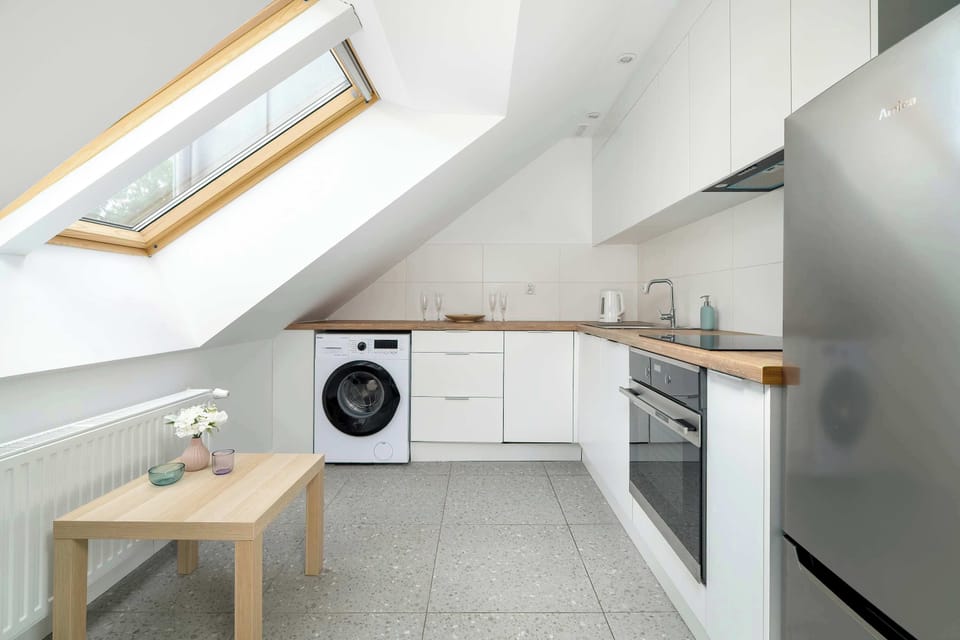 A compact white kitchen tucked under a slanted ceiling, equipped with a fridge and stove. The skylight above the counter provides plenty of daylight.