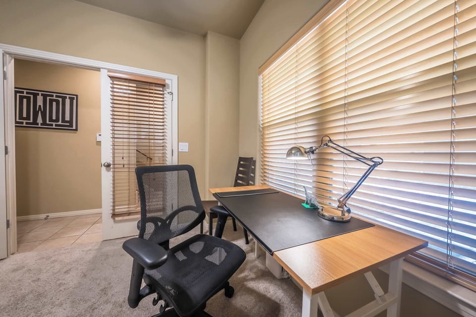 desk with lamp and desk chair with 2 chairs on either side on the desk with entrance to office 