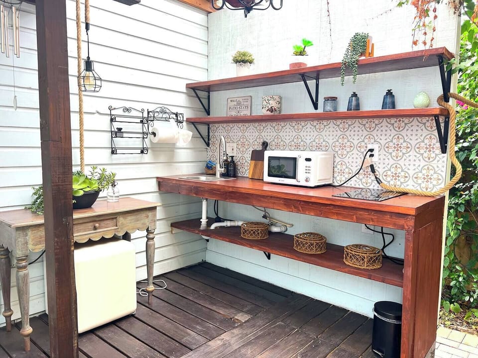 This charming outdoor kitchen makes cooking a breeze with a microwave, hot plate, sink, and thoughtful touches like open shelving and decorative tile. Perfect for preparing meals in the fresh air.