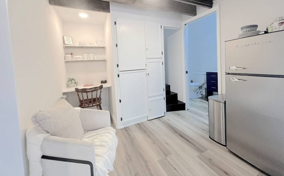 Tucked beneath soft lighting, the built-in desk creates a peaceful nook for reading, journaling, or remote work. Nearby, you’ll find a comfy chair to unwind and a large fridge to keep your essentials on hand.