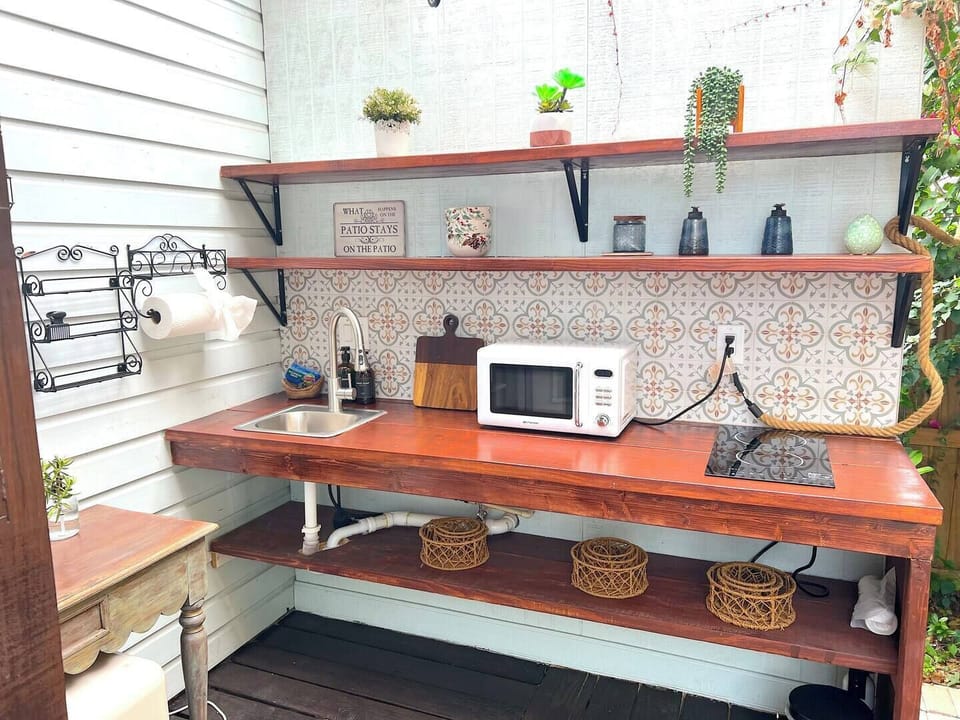 Charming and functional, this outdoor kitchen is equipped with a sink, microwave, and cooktop - ideal for preparing fresh meals al fresco while surrounded by greenery and handmade touches.