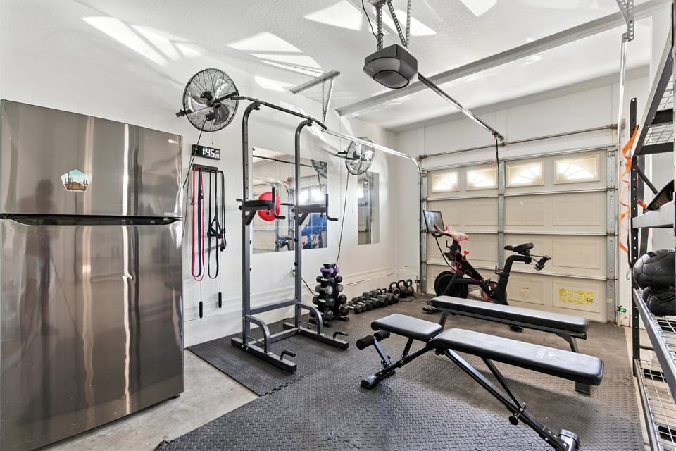 At home gym in the garage with a Peloton bike, bench, pull up bar, and free weights. The Garage also has parking for 2 cars.