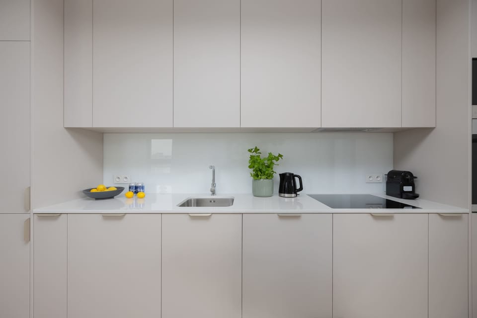 A white kitchen with ample storage, a small plant, and kitchen appliances on the counter.