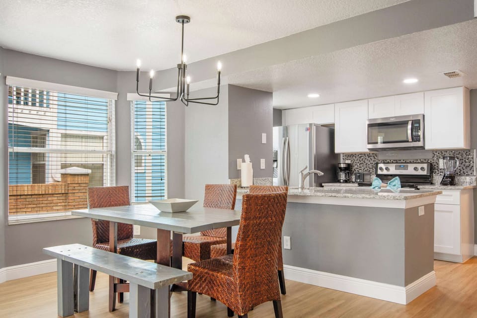 Modern dining with woven chairs, open to a sleek white kitchen. 