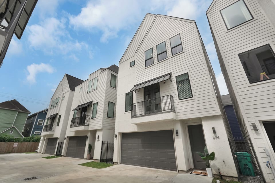 Modern 3-story townhome with a garage, balcony, and sleek white exterior.