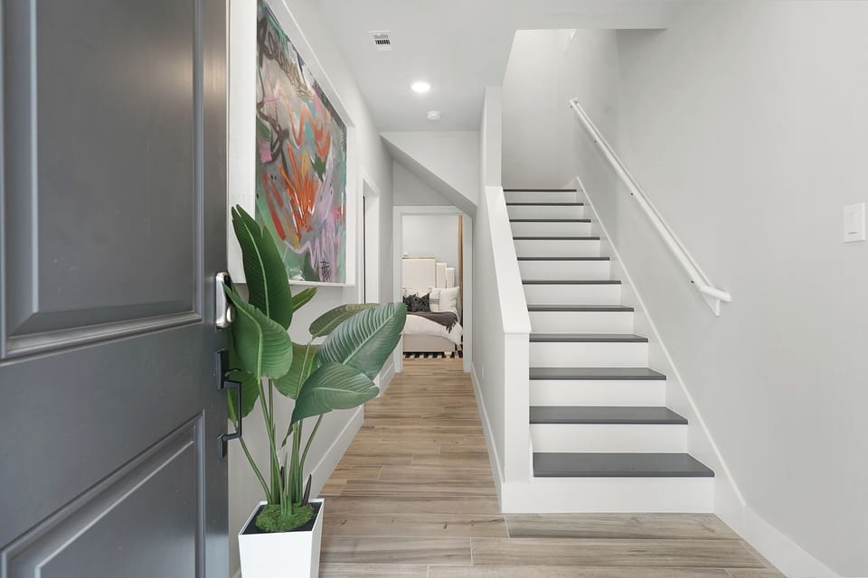 Bright foyer with decorative accents, open stairs, and view into bedroom