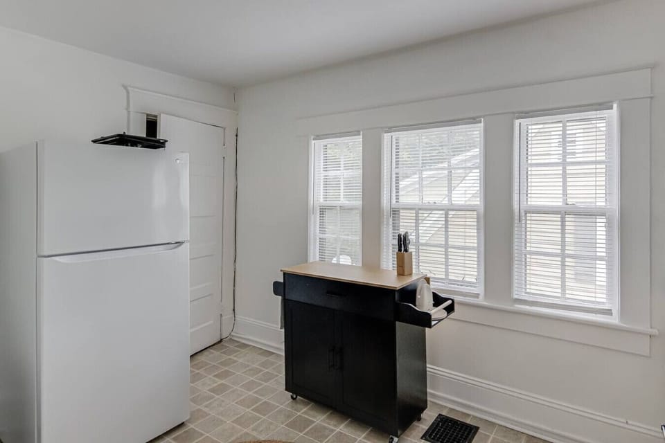 Bright kitchen with a white fridge, black kitchen cart, and three windows.