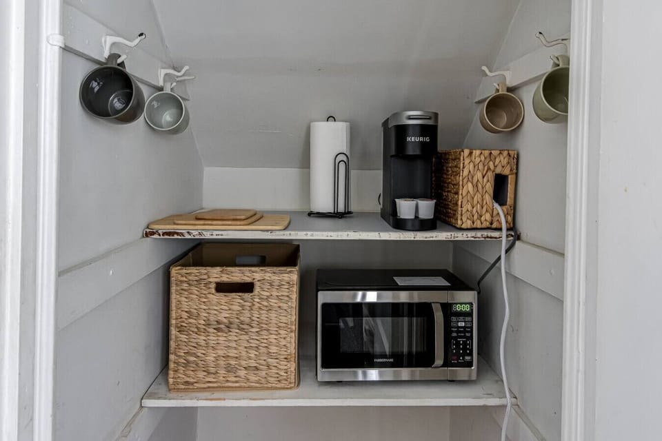 Organized pantry with microwave, coffee maker, and hanging mugs.
