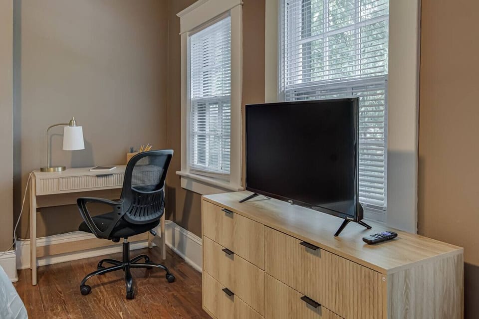 Stylish bedroom featuring a wooden dresser with a TV and a desk area.