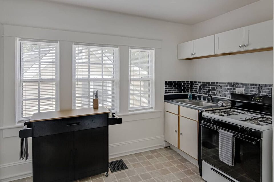 Cozy kitchen with black tiled backsplash, white cabinets, and a kitchen cart.