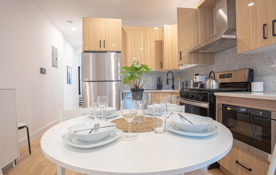 Modern kitchen with dining set for four, sleek appliances, island and pendant lighting.
