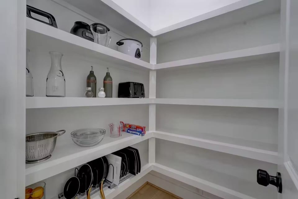 Spacious pantry with cookware, glassware, and appliances neatly organized.