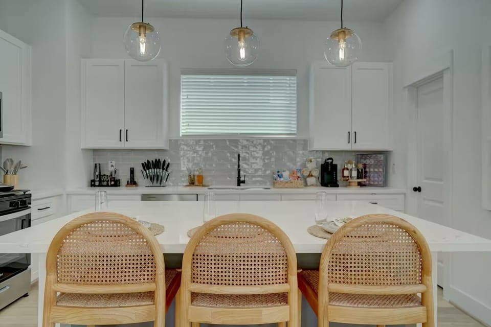 Sleek, bright white kitchen with large island and modern globe lighting.