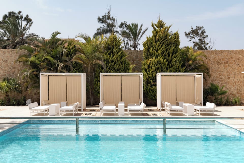Lounge lazily poolside in shaded cabanas beside sparkling water.