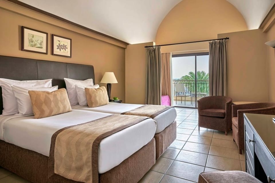 Unwind in twin beds with breezy balcony views beyond.