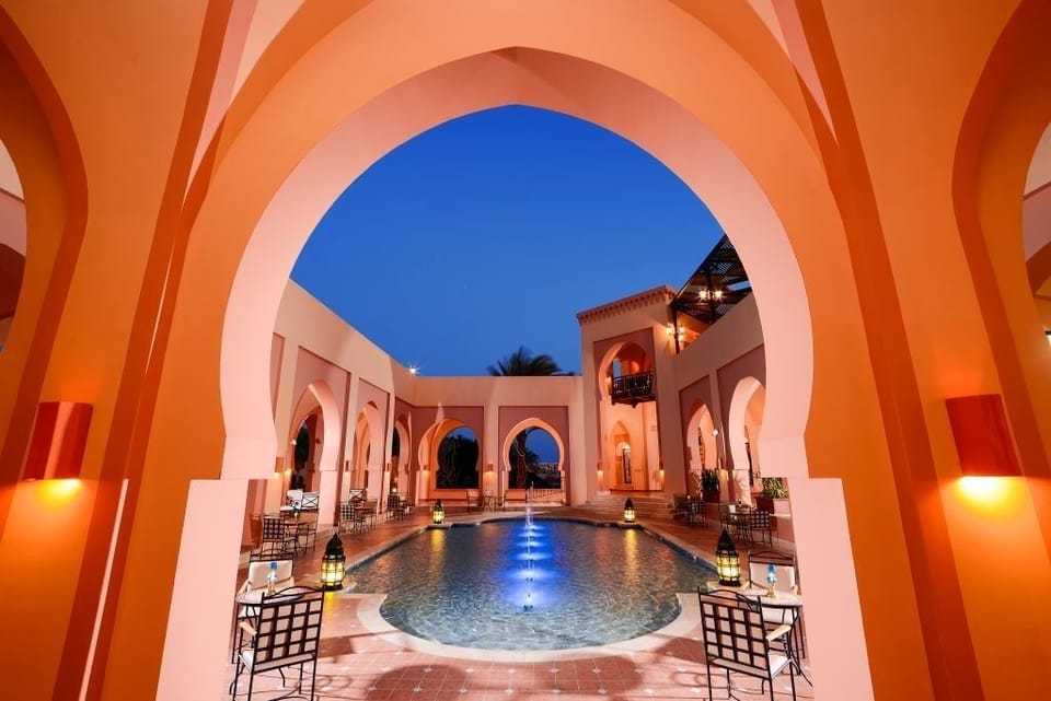 Sip and lounge poolside as arches glow at dusk.