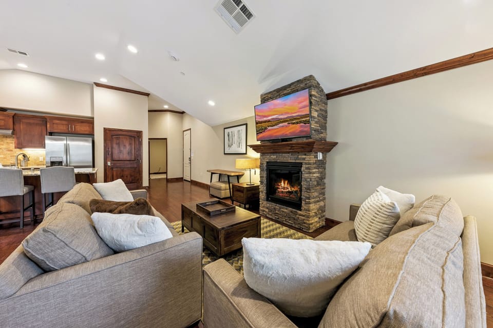 Unwind in your spacious living room where plush sofas face a cozy stone fireplace, perfect for relaxing evenings.