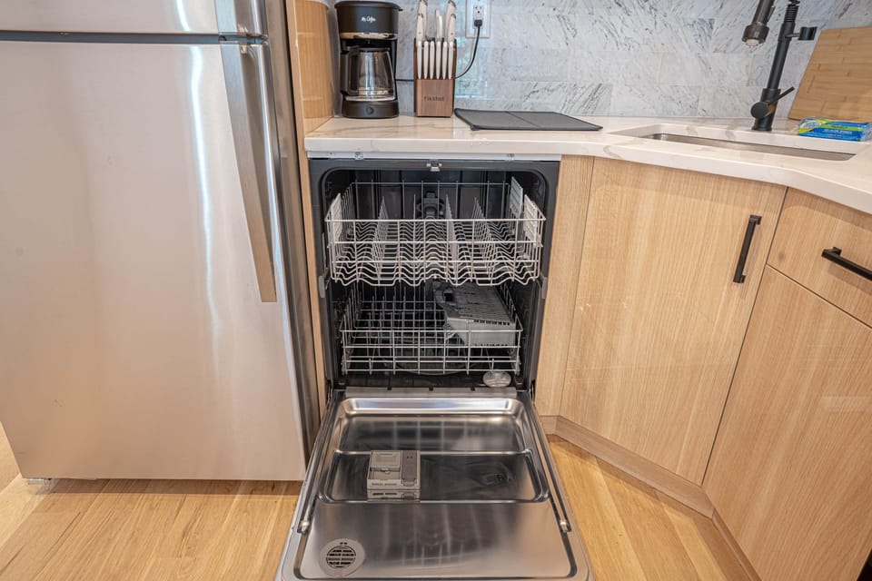 Sleek kitchen with dishwasher, marble backsplash, and stainless steel fridge
