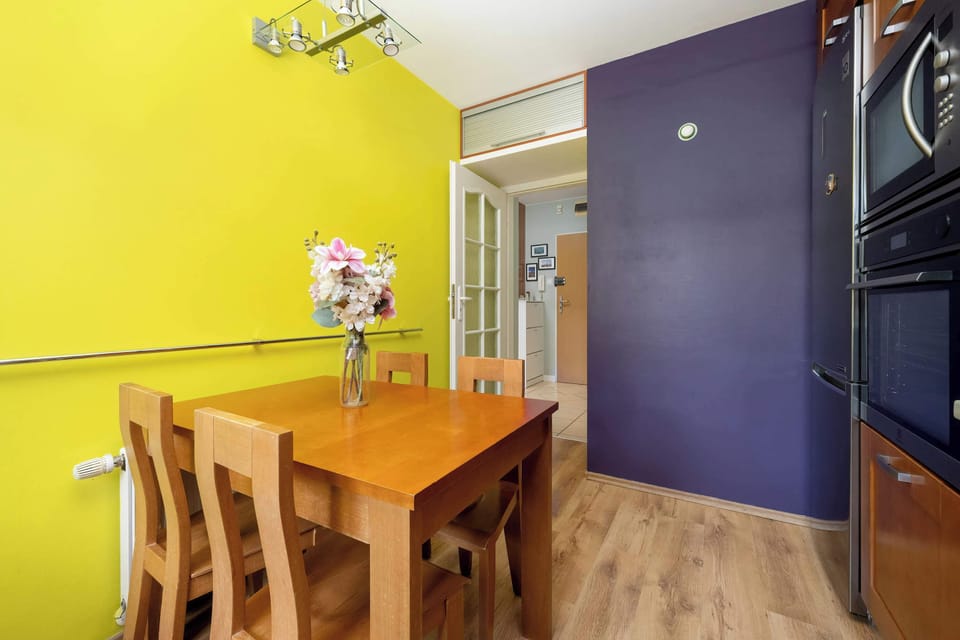 The light wood dining table placed between purple and yellow walls creates a cheerful setting for family meals.