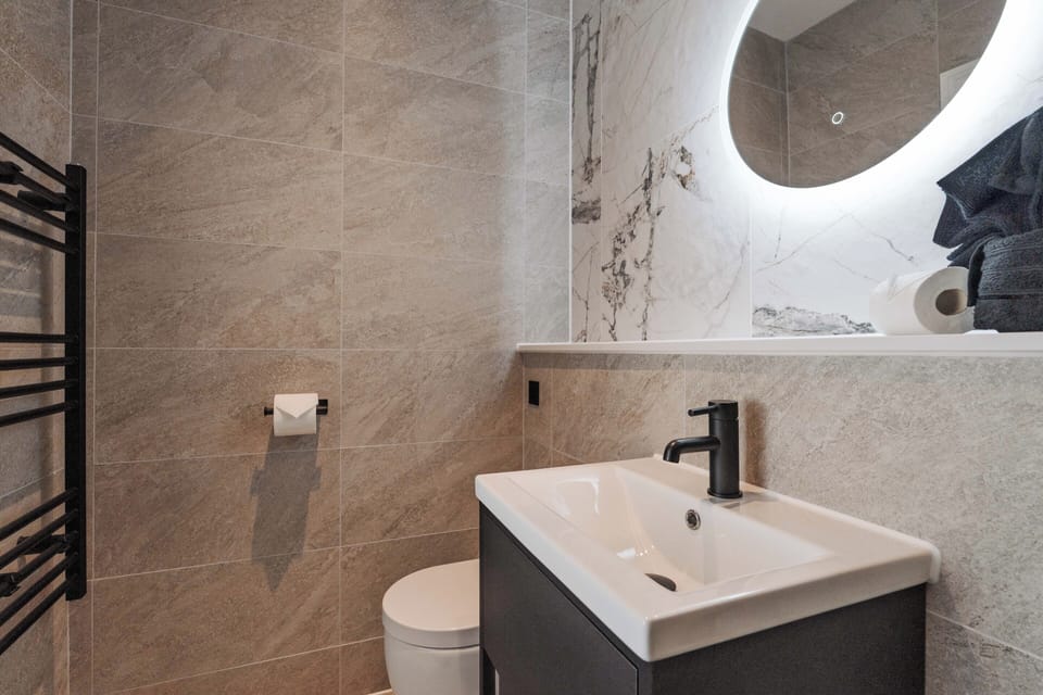A clean, modern bathroom with an electric shower, toilet, sink, and small makeup mirror—providing everything you need to refresh and prepare for the day ahead.