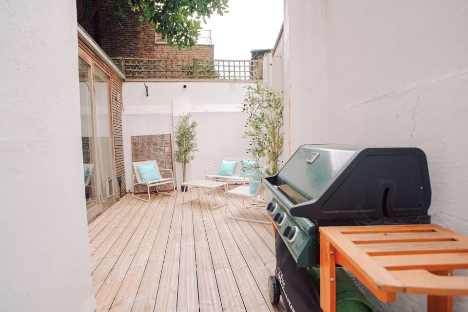 A wooden deck patio with outdoor seating, potted plants, and a barbecue grill.