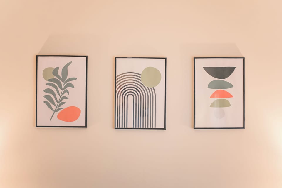 A minimalist trio of framed abstract art pieces decorates the wall. Each print features earthy tones of green, orange, and black with simple shapes—leaves, arches, and stacked forms—adding a modern and calming aesthetic to the space.