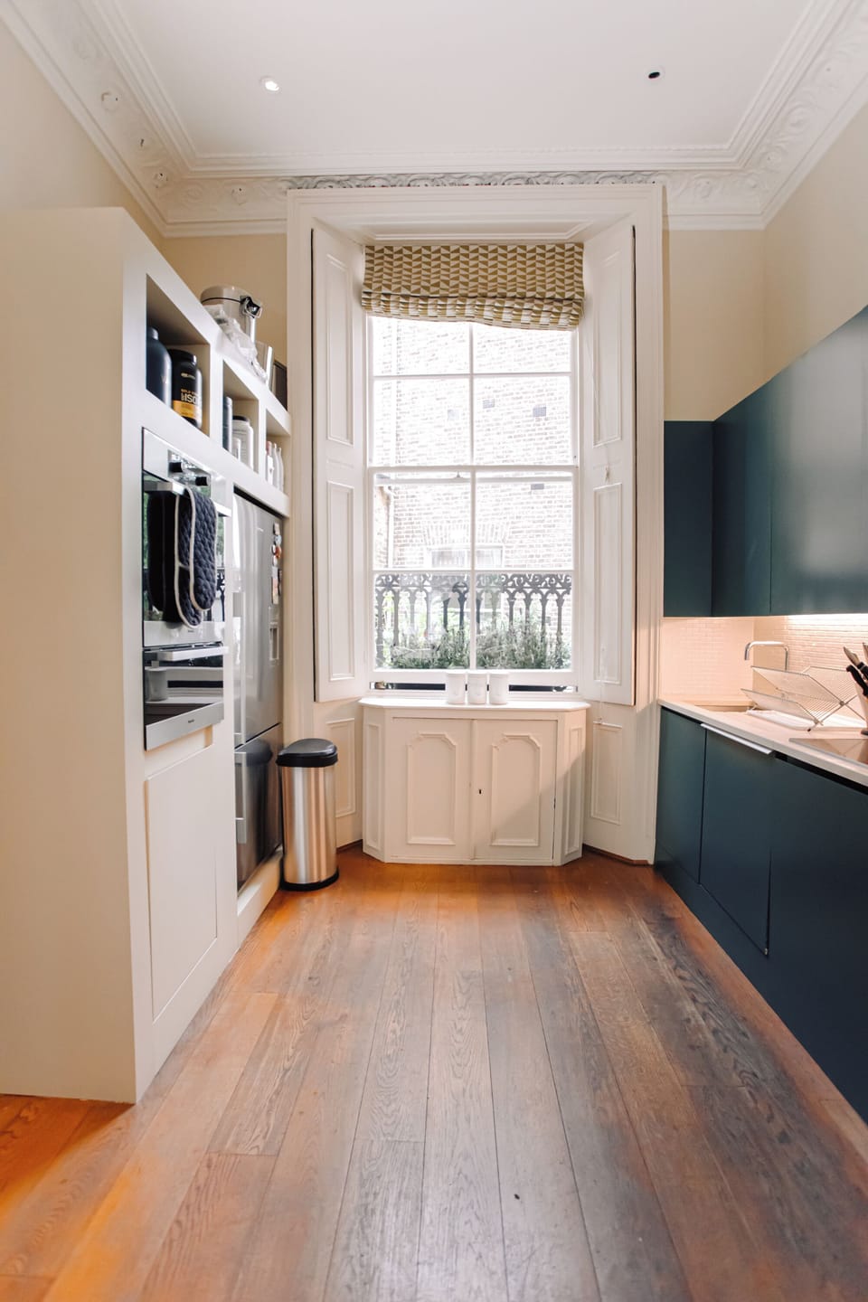 A bright kitchen with dark lower cabinets, built-in appliances, and a large window with a woven blind.