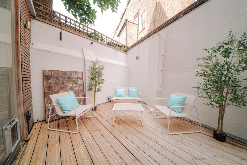 A small patio with white seating, turquoise cushions, and potted plants on wooden decking.
