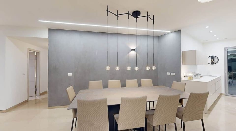 A stunning dining space with a modern concrete accent wall, sleek pendant lighting, and plush, quilted chairs. This inviting area is perfect for intimate dinners or lively gatherings, combining style and comfort effortlessly.