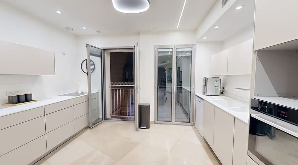 A sleek and modern kitchen featuring high-end appliances, ample counter space, and minimalist cabinetry. Perfect for preparing meals while enjoying access to a view of the Mamilla Promenade below.