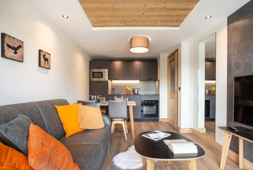 The cozy living area features a modern sofa adorned with vibrant cushions, a stylish dining table, and a well-equipped kitchen, creating a welcoming atmosphere for family gatherings.
