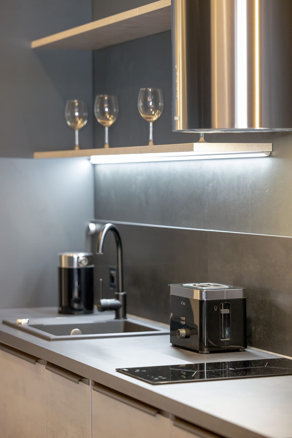 A kitchen counter with small appliances, including a coffee maker. The sleek surfaces reflect the under-cabinet lighting.