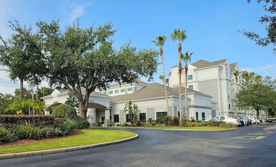The property features tropical landscaping, well-lit walkways, and a welcoming lobby entrance.