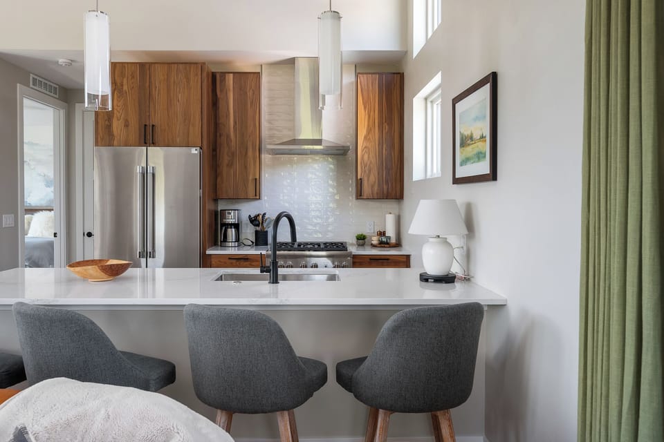 - Sleek kitchen with stainless steel fridge and stove   - Modern island with bar seating and pendant lighting   - Bright windows bring in natural mountain light