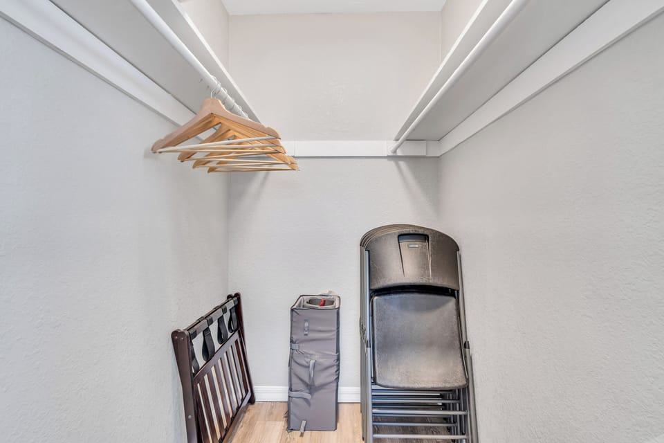 Master bedroom walk-in closet with plenty of clothing storage space and a few hangers. There is also a pack-n-play and some extra folding chairs.
