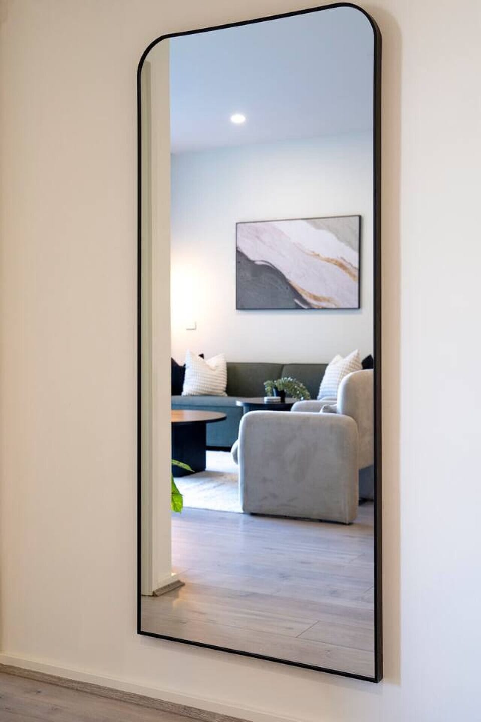 Full length designer mirror reflecting the stylish living area, adding depth and light to the space. Perfect for getting ready or adding a modern touch to the apartment’s clean, elegant design.